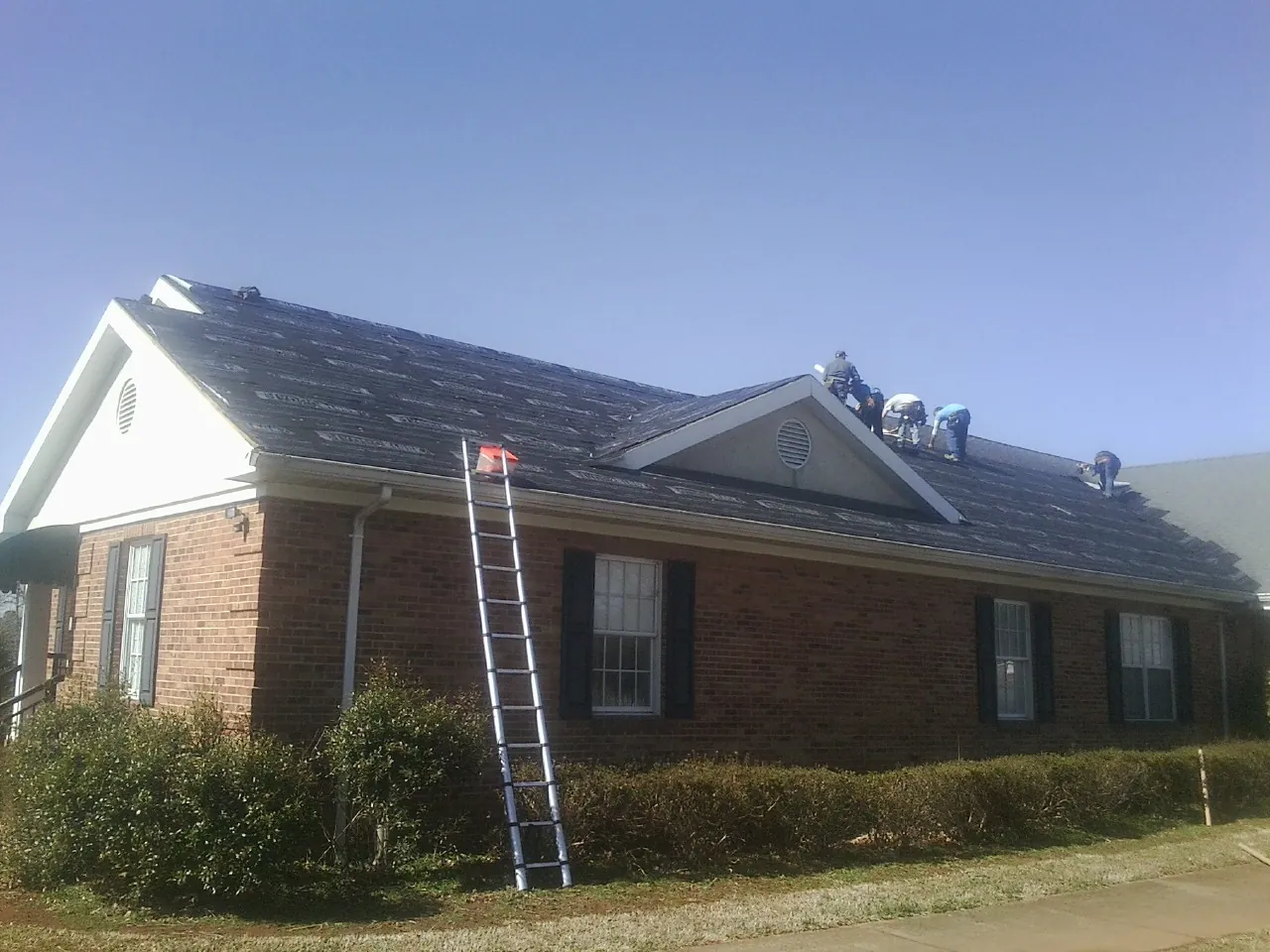 Crew tearing shingles off a brick ranch roof with a ladder set — Metal Roof Repair work by our crew in Bonney Lake