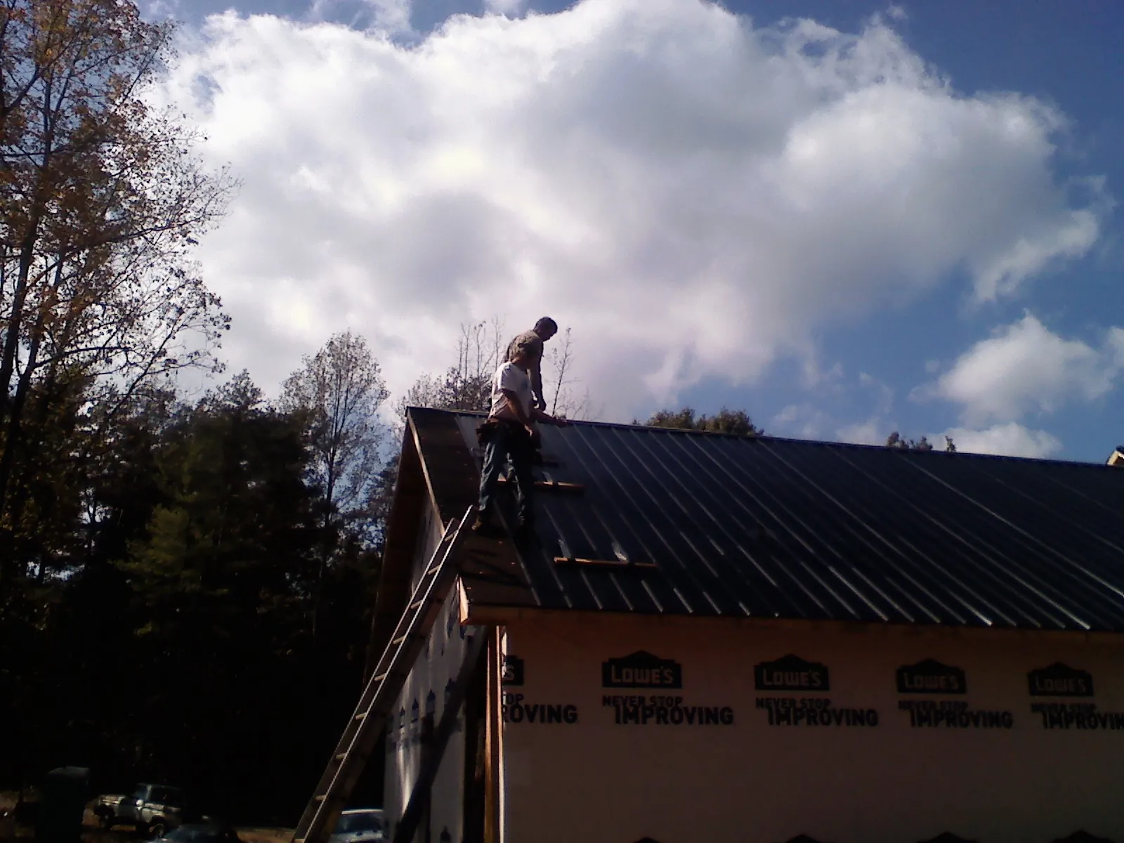 Roofer fastening dark metal panels high against a cloudy sky, from a Roof Inspection job in Bonney Lake