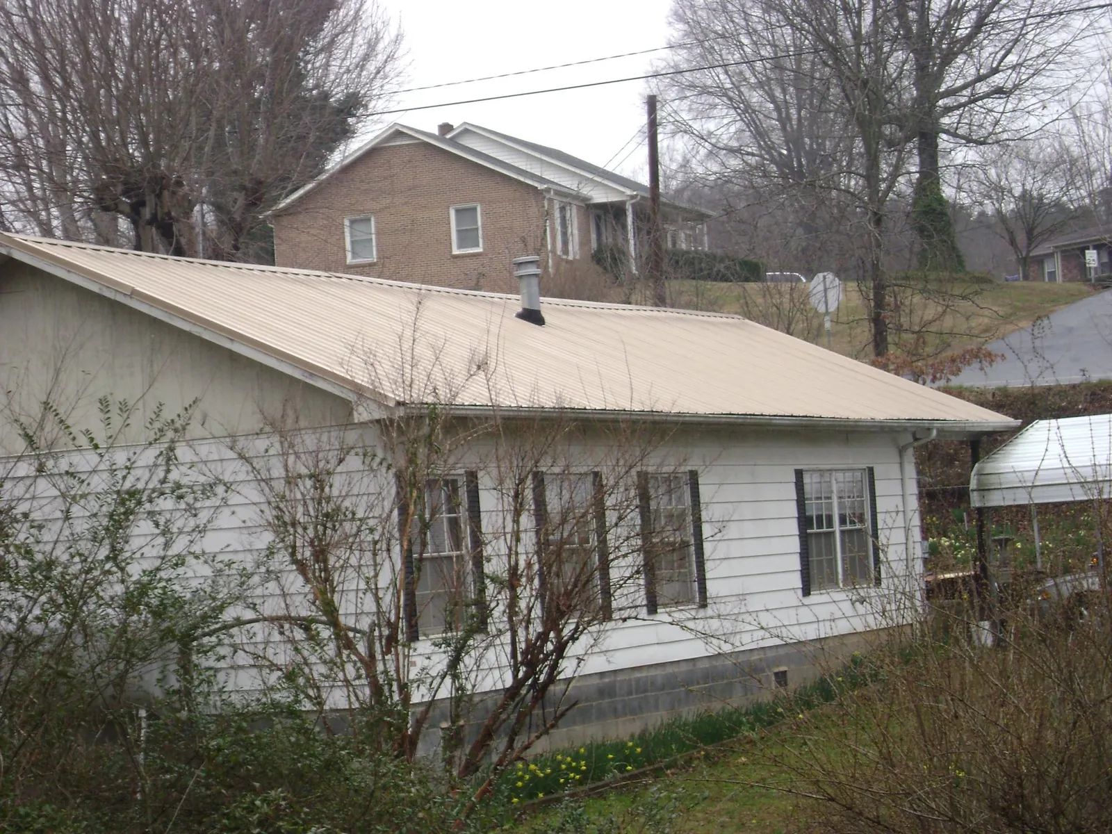 Tan metal roof on a white sided house set into a hillside — Commercial Roofing by Roofing Brothers in Bonney Lake